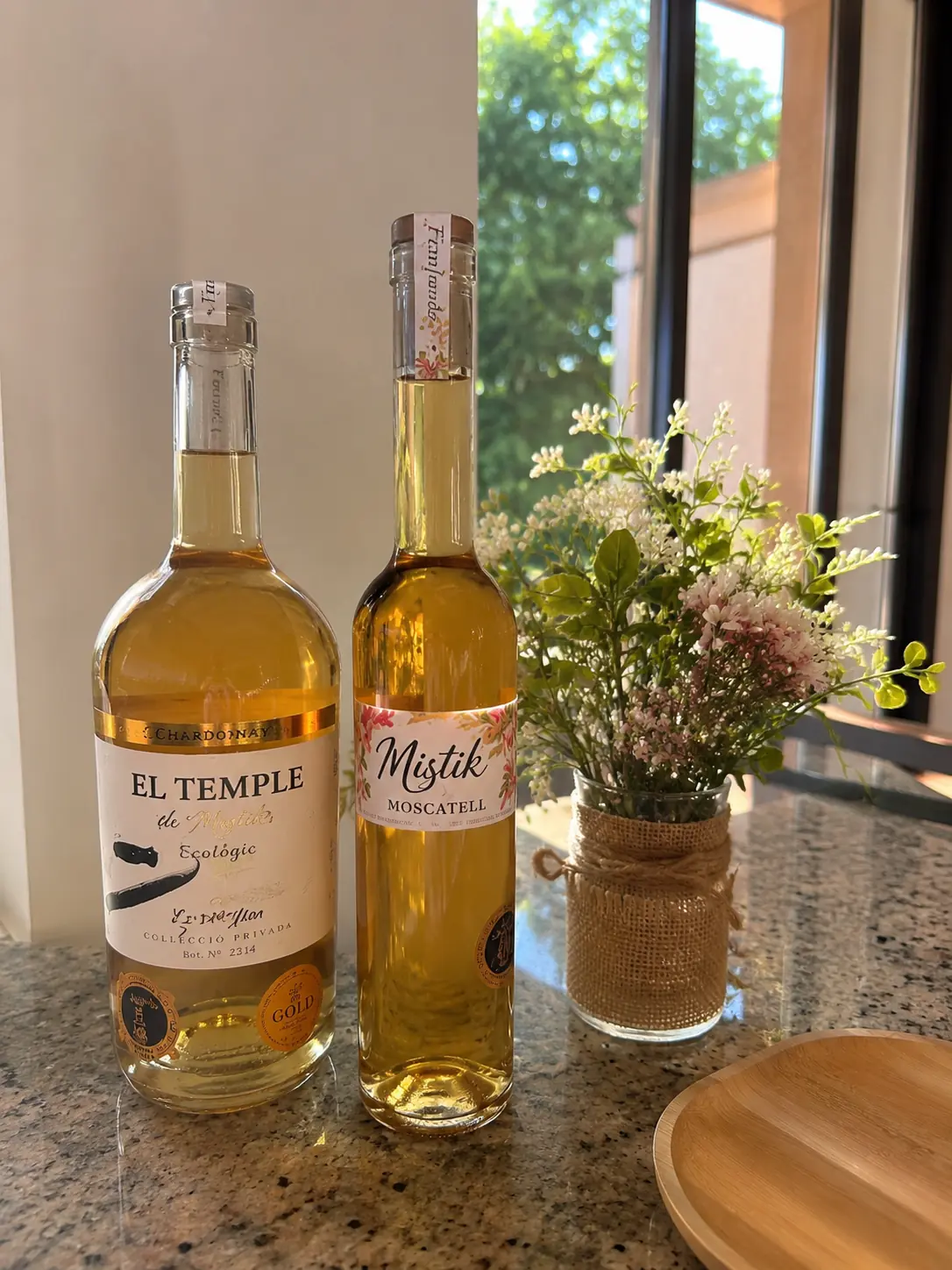 Botellas El Temple de Mistik Ecològic y Mistik Moscatell, vinos blancos ecológicos de Alkimia Wines, junto a una ventana